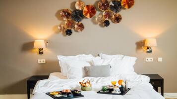 Een hotelkamer met een bed, kussens, nachtkastjes, wandlampen en een dienblad met ontbijtartikelen.