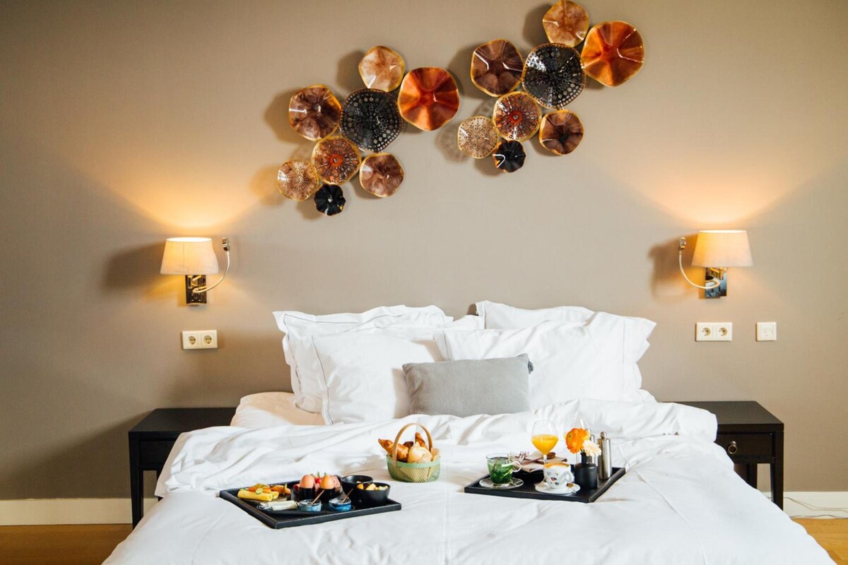 A hotel room with a bed, pillows, bedside tables, wall-mounted lamps, and a tray with breakfast items.