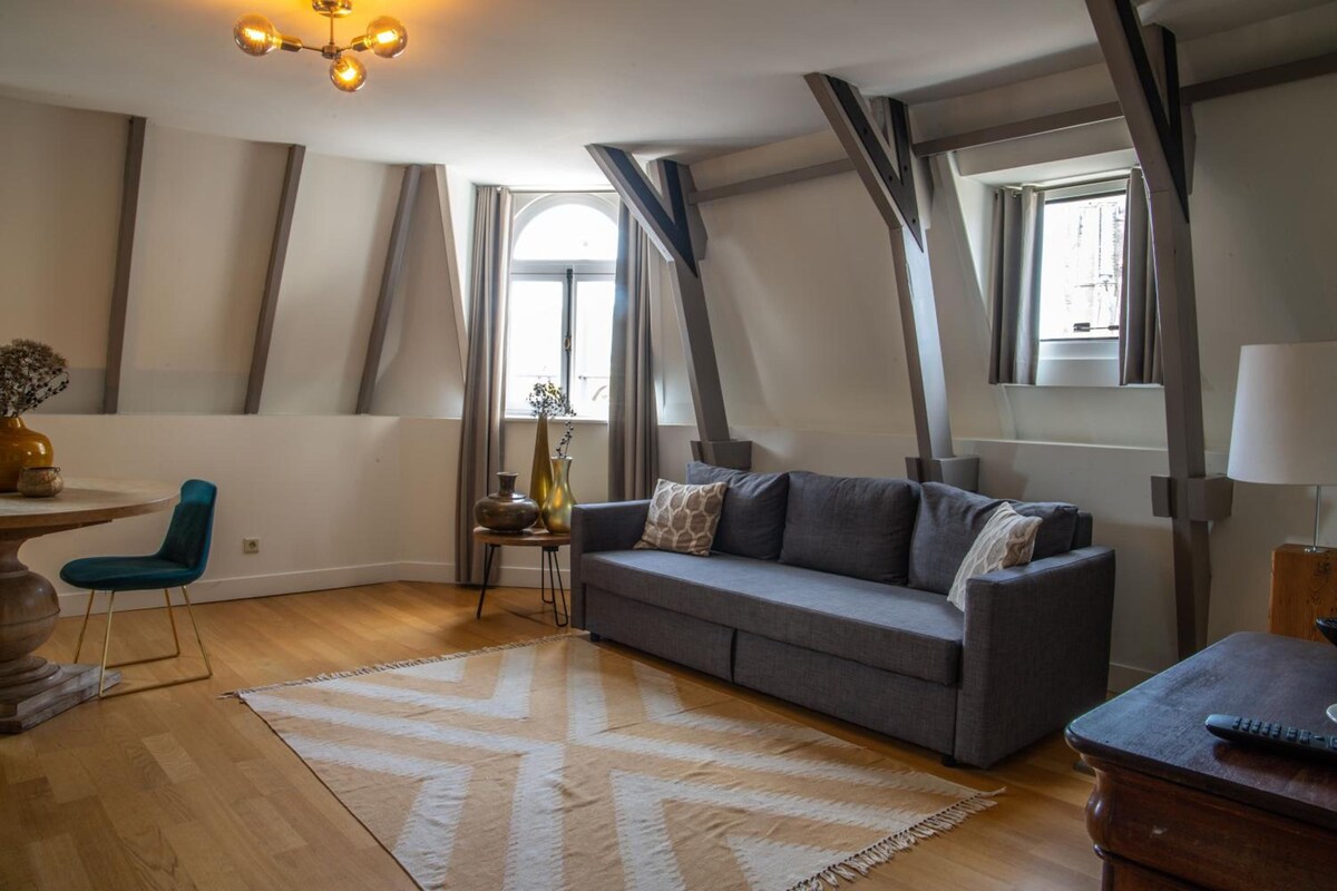 A modern living room with a grey sofa, wooden flooring, and a patterned rug.