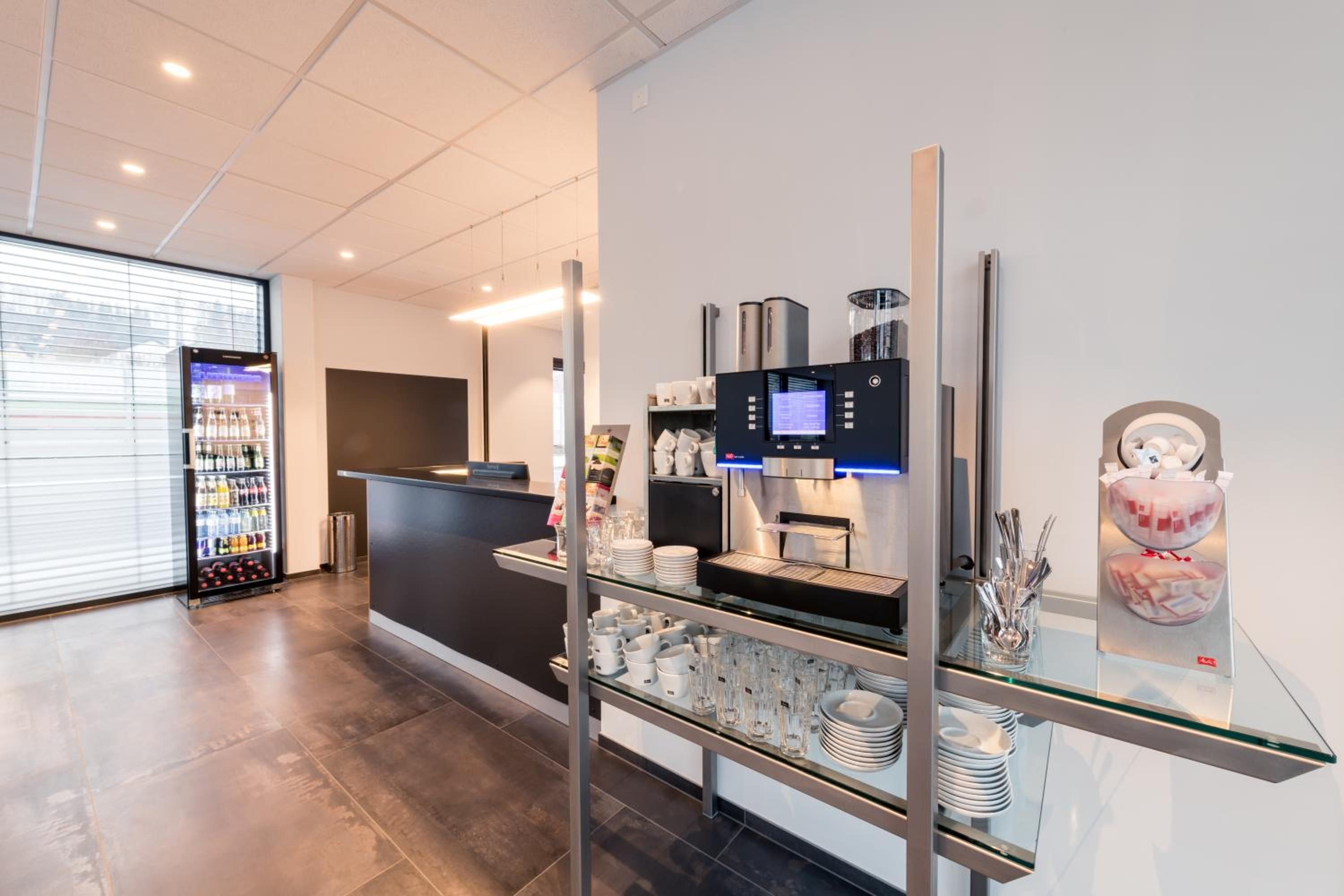 Ein moderner Empfangsbereich mit einer Selbstbedienungs-Kaffeestation, einem Getränkeautomaten und einer Glastheke für Besteck.