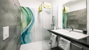 Un bany modern amb un plat de dutxa de vidre, un mirall gran i un lavabo blanc sobre un taulell negre.