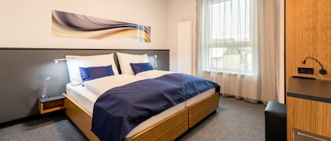 Habitación de hotel con cama, mesita de noche, lámpara, un amplio ventanal con cortinas y un armario de madera.
