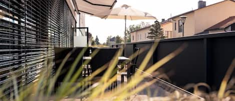 An outdoor patio area with a table and chairs under a canopy, surrounded by a fence and vegetation.