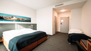 A hotel room with a bed, a bedside table, a chair, a desk, and a painting of a cityscape.