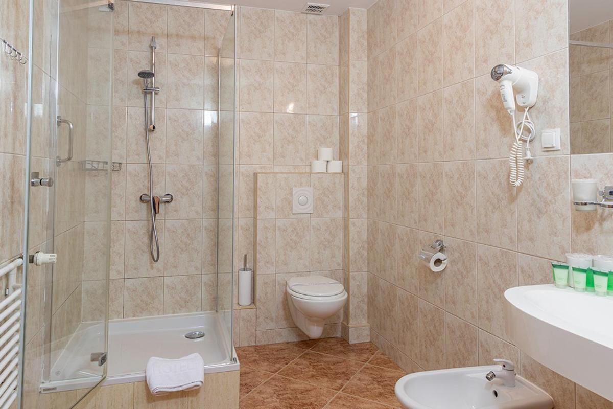 Un baño con ducha de vidrio, inodoro, lavamanos y secador de pelo montado en la pared.