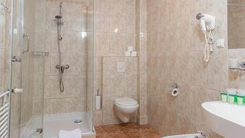 A bathroom with a glass-enclosed shower, a toilet, a sink, and a hairdryer mounted on the wall.