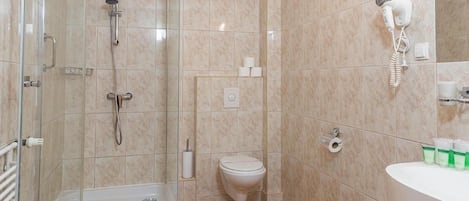 Un baño con ducha de vidrio, inodoro, lavamanos y secador de pelo montado en la pared.