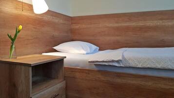 A single bed with a wooden headboard, a bedside table with a lamp, and a small vase with a flower.