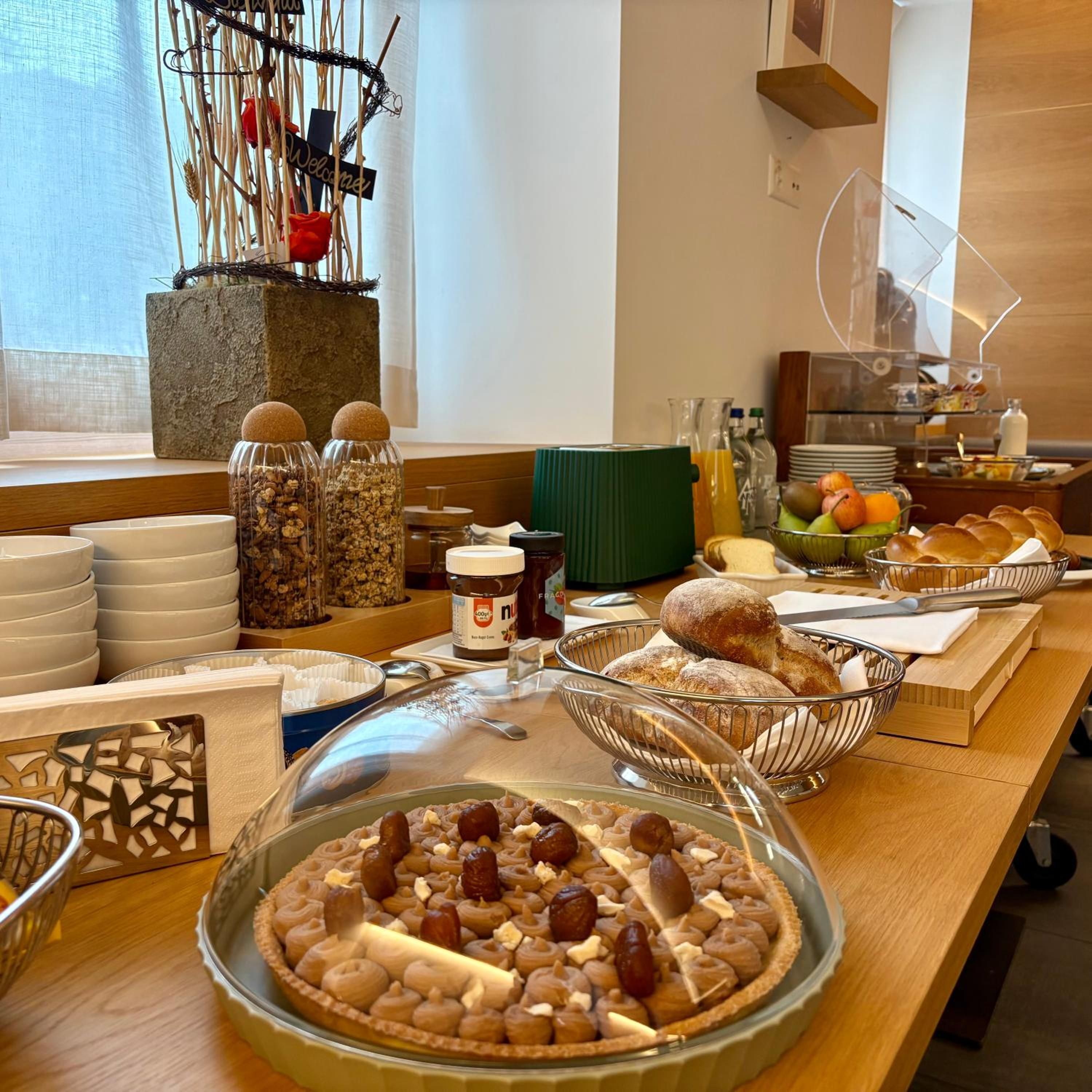 Ein reichhaltiges Frühstücksbuffet mit verschiedenen Speisen, darunter ein Kuchen mit Nüssen und Trockenfrüchten, Brot und einer Auswahl an Getränken.