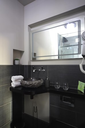Un baño moderno con un lavamanos negro, un espejo y un secador de pelo.