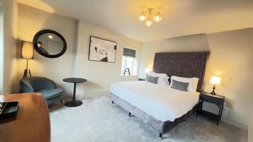 Una habitación de hotel con una cama grande, un espejo redondo, una mesita pequeña, una silla y una lámpara.