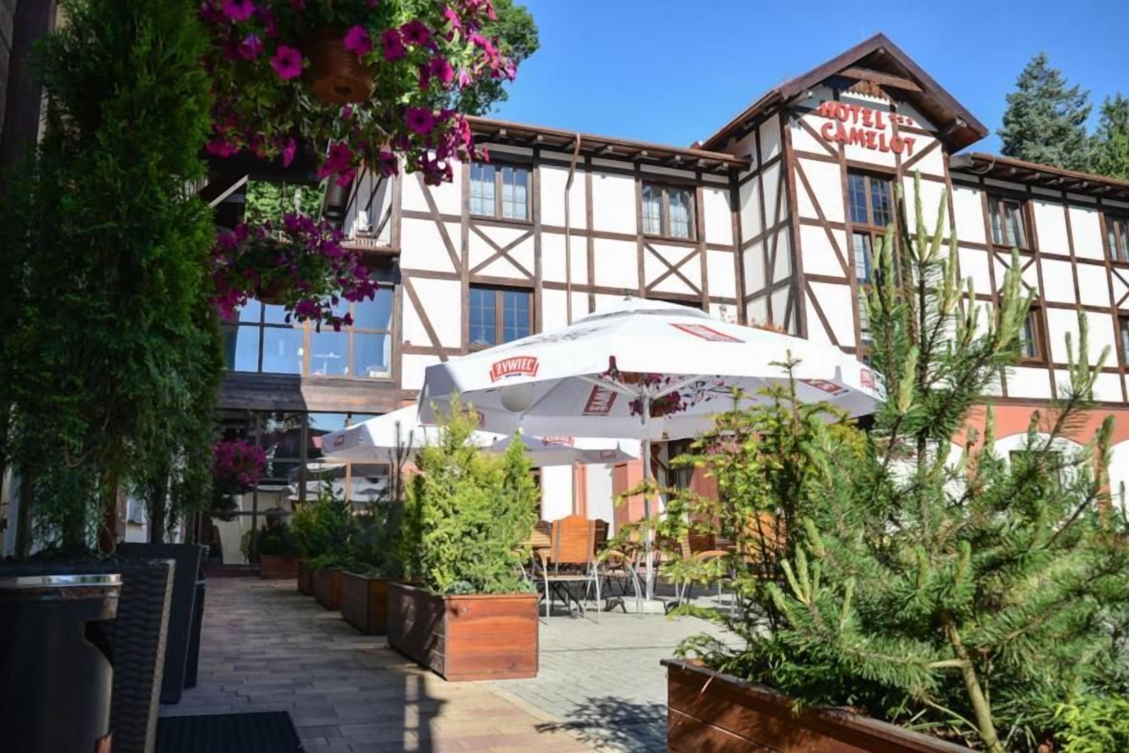 A hotel with a traditional European architectural style, featuring a balcony with outdoor seating and hanging flower baskets.