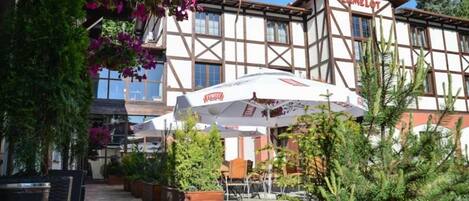 A hotel with a traditional European architectural style, featuring a balcony with outdoor seating and hanging flower baskets.