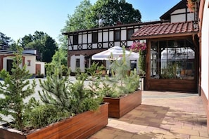Une cour agrémentée de jardinières en bois, un bâtiment traditionnel avec un toit en tuiles et une entrée avec une porte en verre.