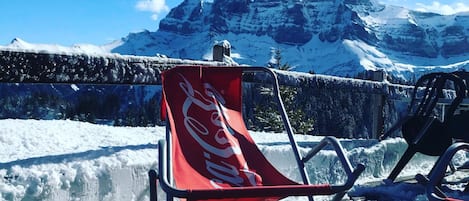 En stol med Coca-Cola logo, en kop med måne og stjernedesign, og en rød askebæger på en moler med et snedækket bjerg i baggrunden.