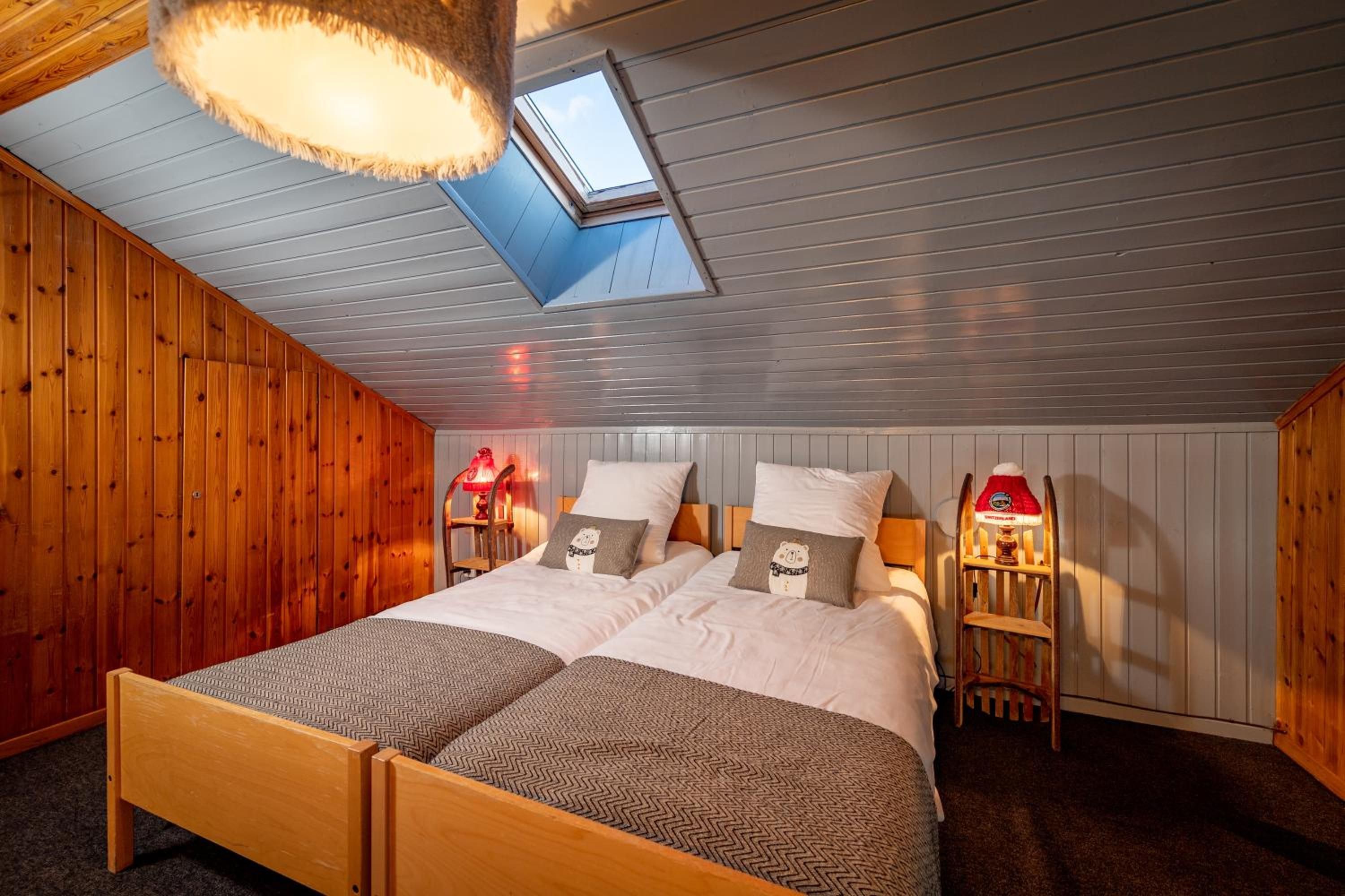 A bedroom with a wooden bed, two bedside lamps, a skylight, and a view of the sky.