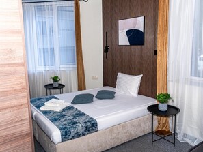 Quarto de hotel com cama, mesa de cabeceira, obra de arte na parede e janela com cortinas.