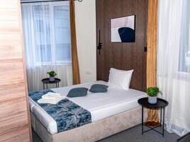 Habitación de hotel con cama, mesita de noche, una obra de arte en la pared y ventana con cortinas.