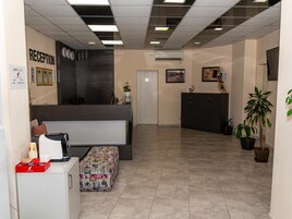 Un área de recepción con mostrador, máquina de café, zona de estar con reposapiés estampado y una puerta numerada con el número 6.