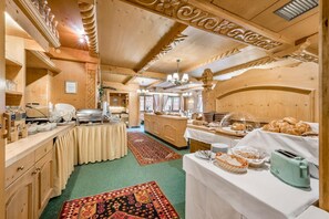 A wooden interior with a buffet setup, including a buffet table, serving area, and a kitchen in the background. - Pension Almrausch (Neustift Im Stubaital)