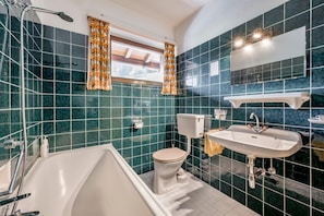 A bathroom with a bathtub, toilet, and sink, featuring teal tiles and a window with curtains. - Pension Almrausch (Neustift Im Stubaital)