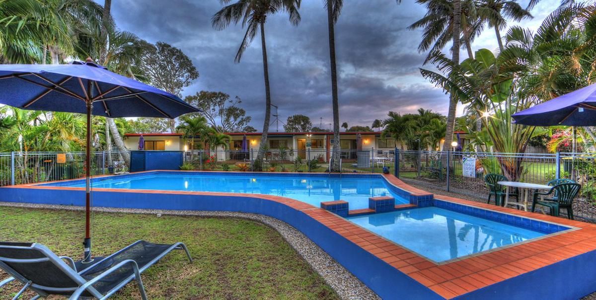 A swimming pool with a blue tiled edge, surrounded by a grassy area and palm trees.