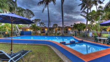 A swimming pool with a blue tiled edge, surrounded by a grassy area and palm trees.
