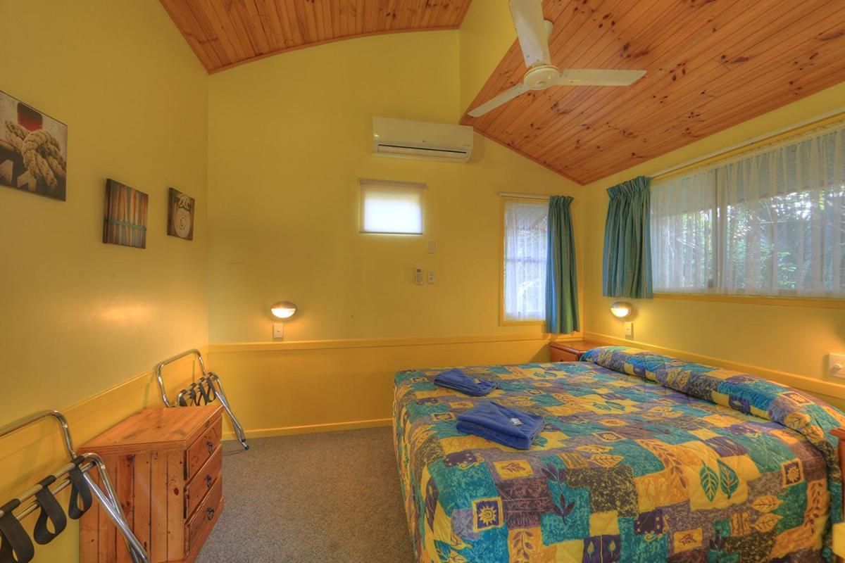 A room with a bed, a wooden dresser, a ceiling fan, and a window with curtains.