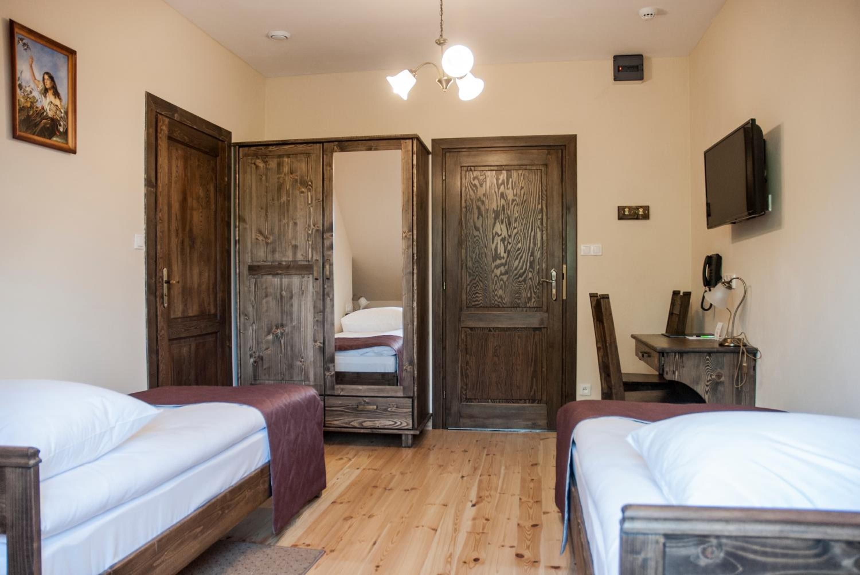 A room with two beds, wooden doors, a television, and a desk with a chair.