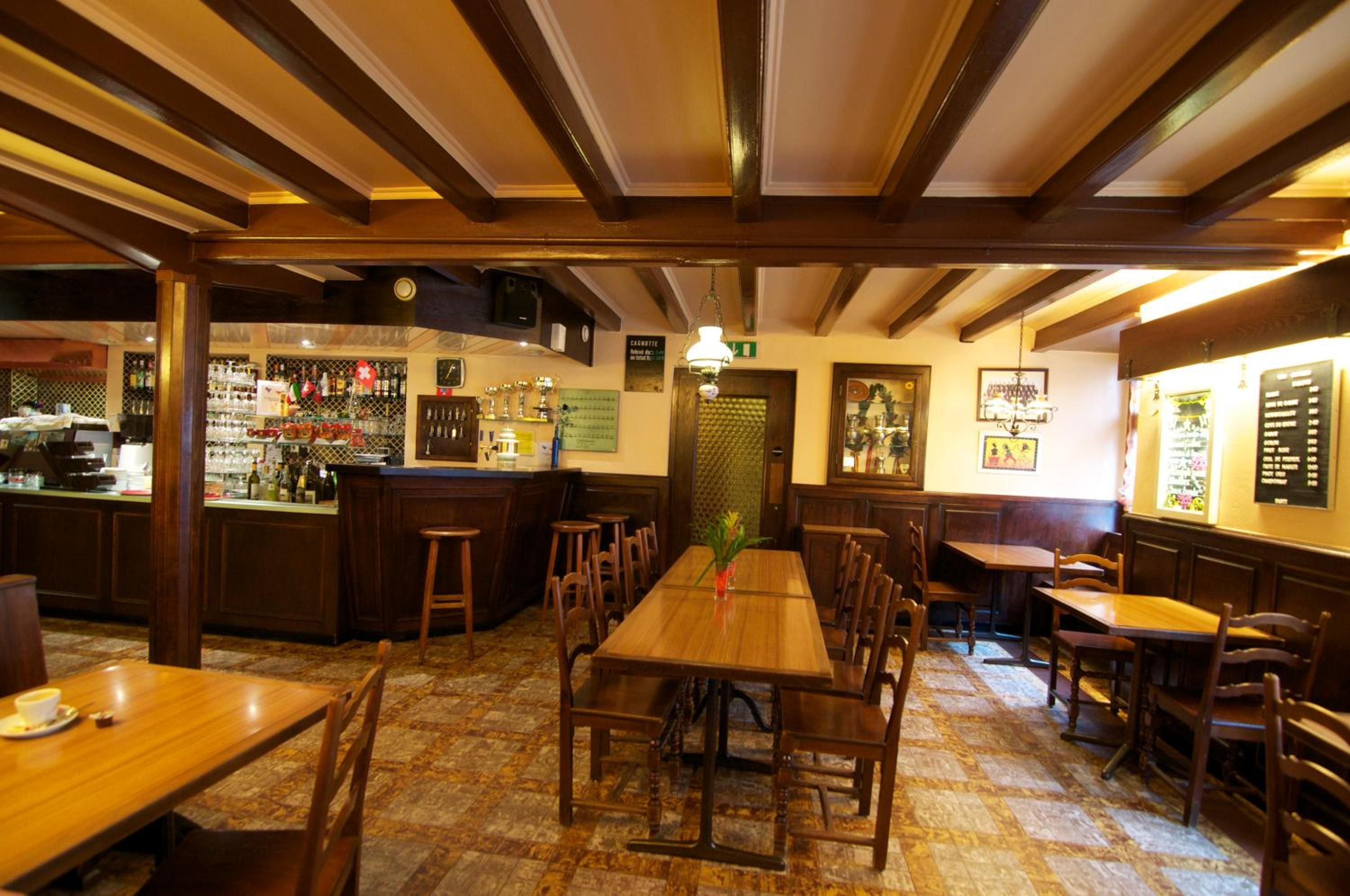 A restaurant interior with wooden tables and chairs, a bar area with bottles, and a patterned floor.