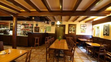 A restaurant interior with wooden tables and chairs, a bar area with bottles, and a patterned floor.
