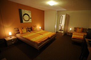 A hotel room with a double bed, two bedside tables, a nightstand, a mirror, and a door leading to another room. - Hv Tel De La Croix Blanche (Cressier)