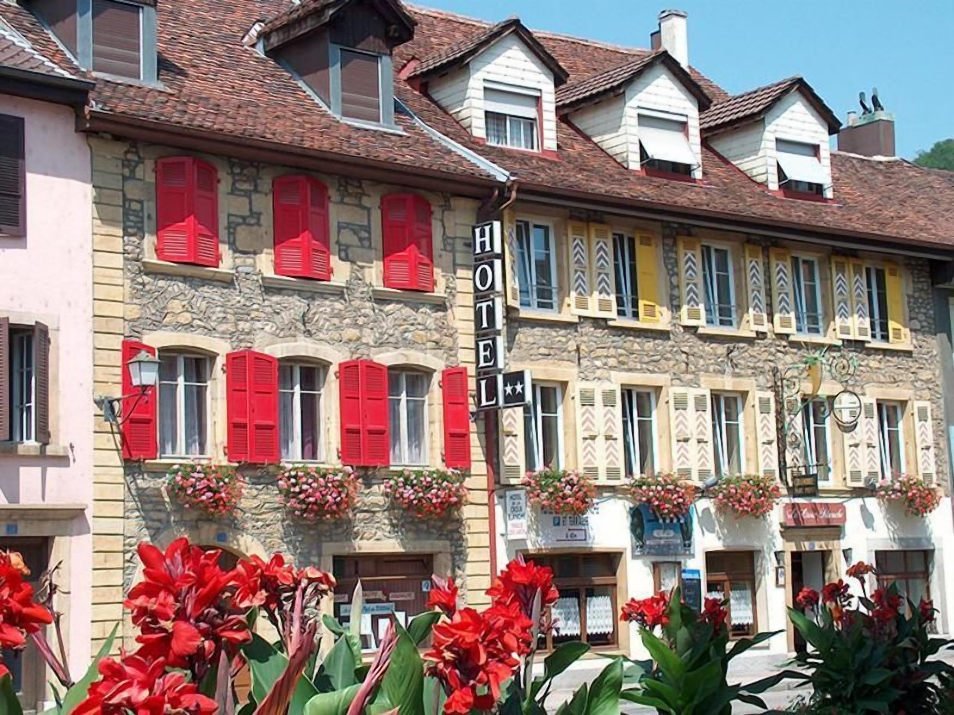 A hotel with multiple stories, red shutters, and flower boxes on the facade.