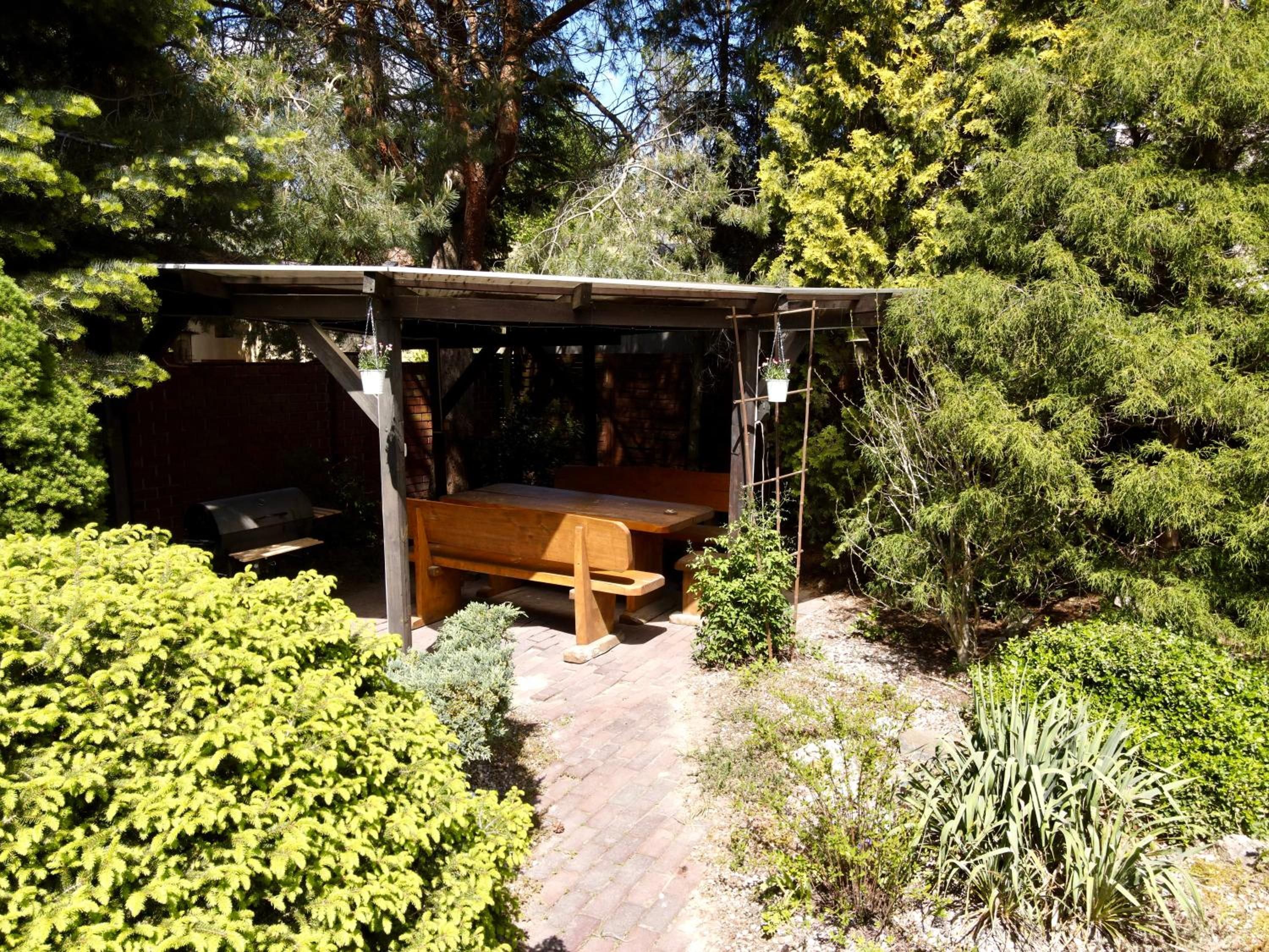 A covered outdoor seating area with a wooden bench and a grill.