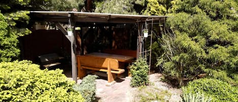 A covered outdoor seating area with a wooden bench and a grill.