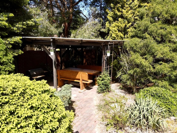 A covered outdoor seating area with a wooden bench and a grill. - Pokoje Rezydencja Parysa (Lublin)