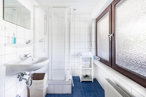 Een badkamer met een douche, wastafel en een raam met gezandstraald glas.