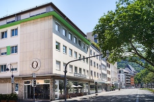 A multi-story hotel with a green and beige facade, multiple windows, and a visible entrance with a sign.