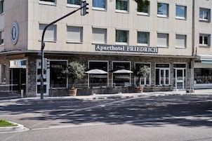 An exterior of an apartment hotel named 'Aparthotel FRIEDRICH' with outdoor seating and a storefront.