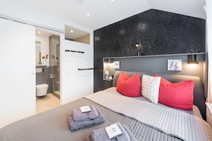 Un dormitorio moderno con una cama grande, cabecera con luces empotradas en la pared, y baño a la vista con inodoro y ducha.