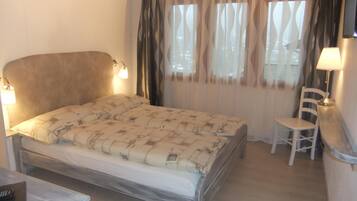A bed with a headboard, two bedside lamps, a chair, a desk, and a window with curtains.