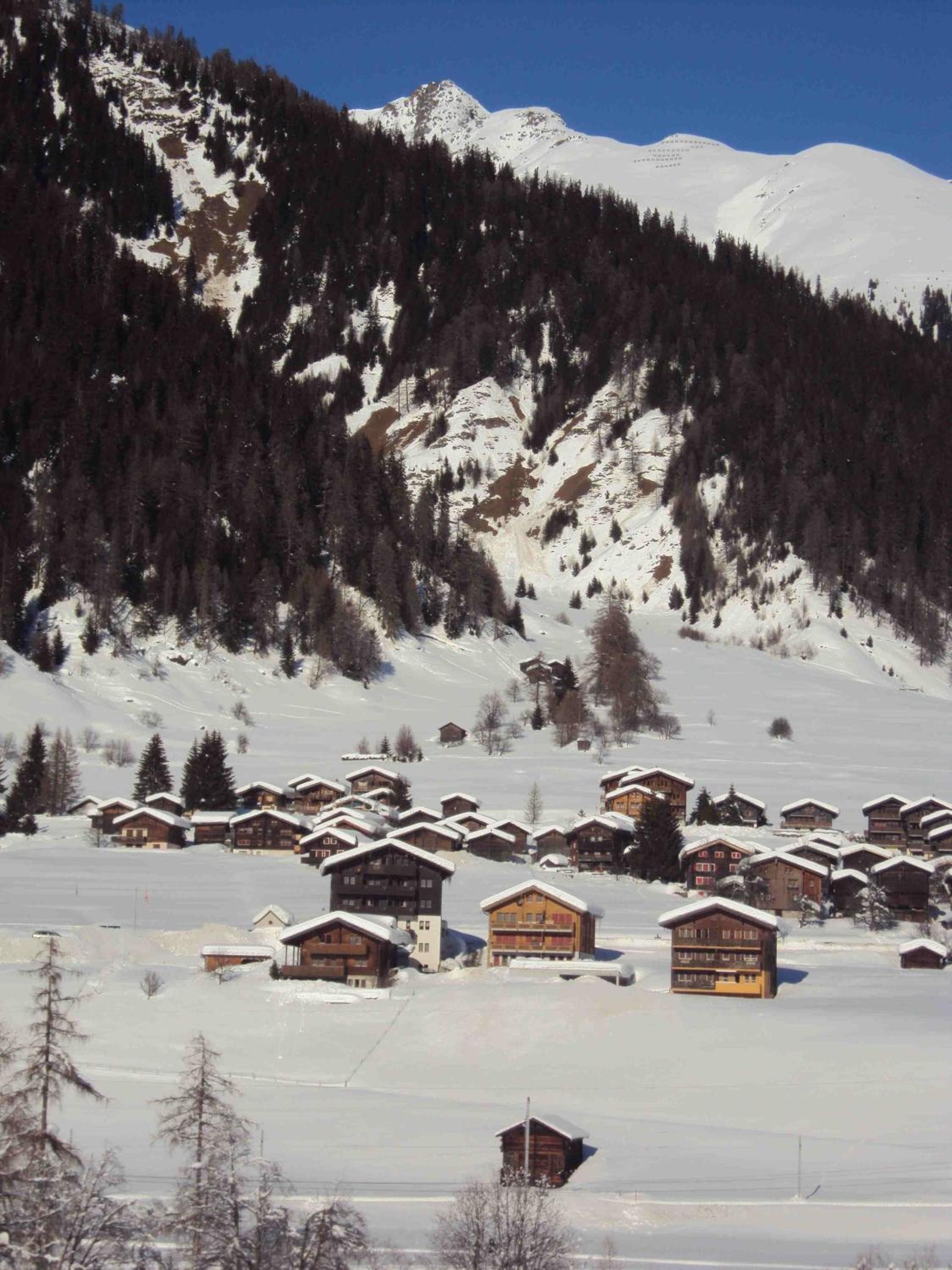 A snow-covered mountain with a cluster of wooden cabins.