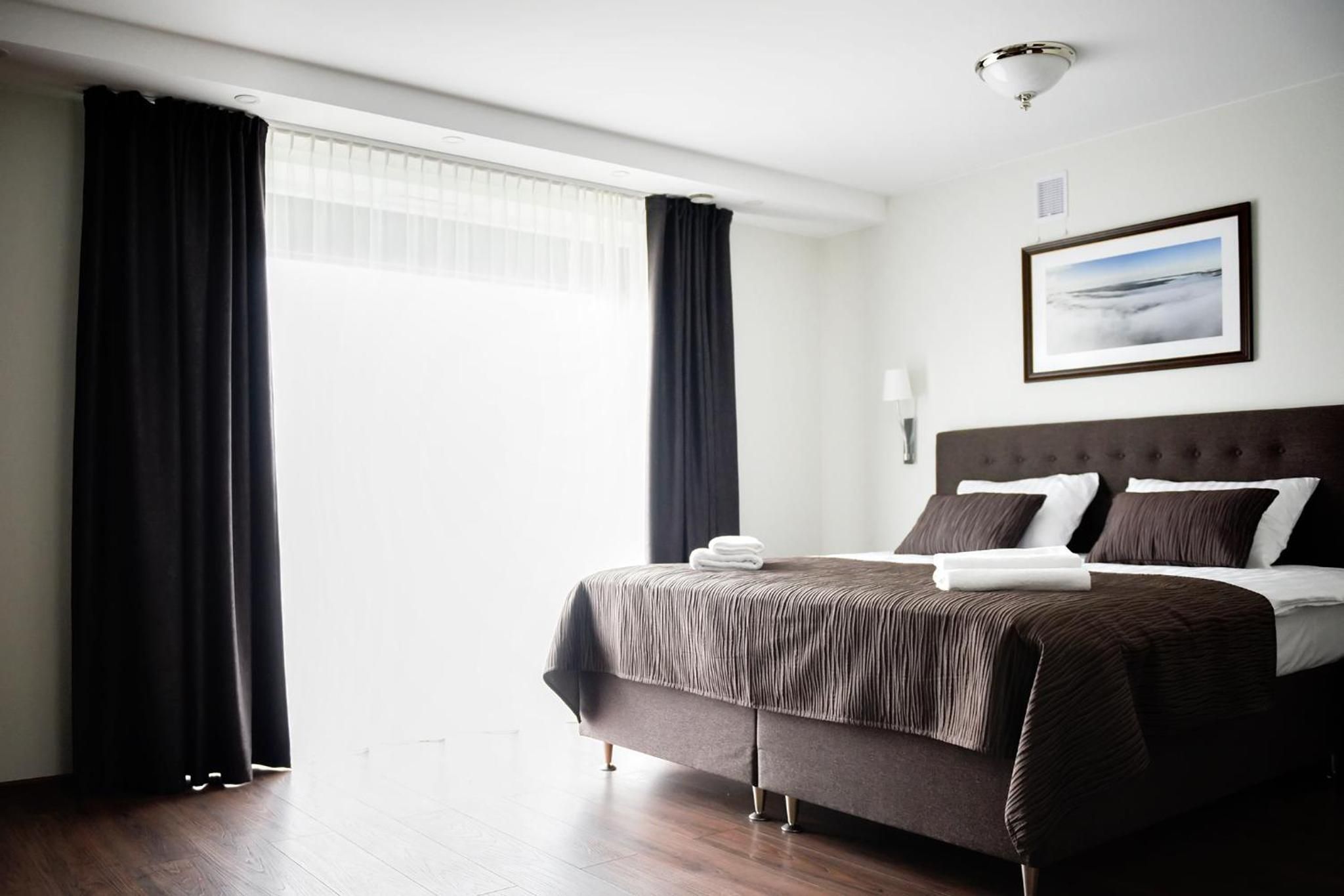 Ein Hotelzimmer mit einem großen Bett, dunklen Vorhängen, einem gerahmten Bild an der Wand und einer Deckenleuchte.