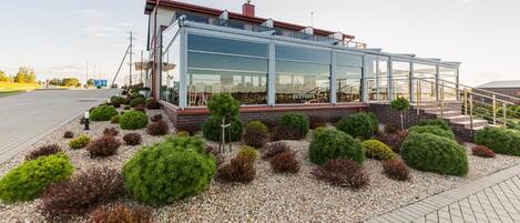 A modern building with a glass facade, a brick base, and a landscaped garden with various shrubs.