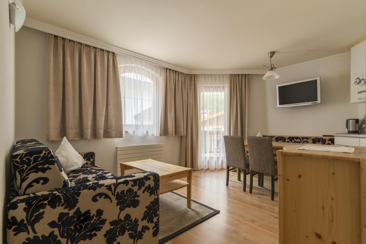 Un espacio habitable funcional con sofá, mesa de comedor, silla, televisor y kitchenette.