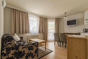A compact living space with a sofa, a dining table, a chair, a TV, and a kitchenette. - Hotel Garni Chasa Nova (Samnaun)