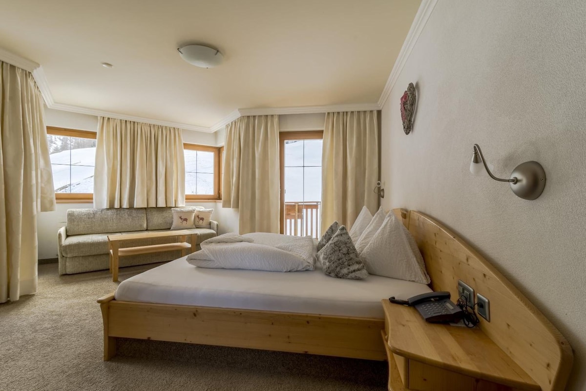 Un dormitorio con una cama de madera, una mesita de noche de madera, un teléfono y una ventana con cortinas.