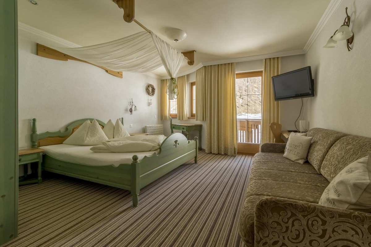 Una habitación con cama, sofá, televisión y ventana con cortinas.
