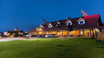 A hotel with a red roof and multiple windows, a parking lot with several cars, and a well-maintained lawn.