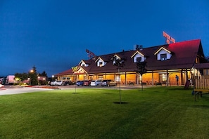 A hotel with a red roof and multiple windows, a parking lot with several cars, and a well-maintained lawn.